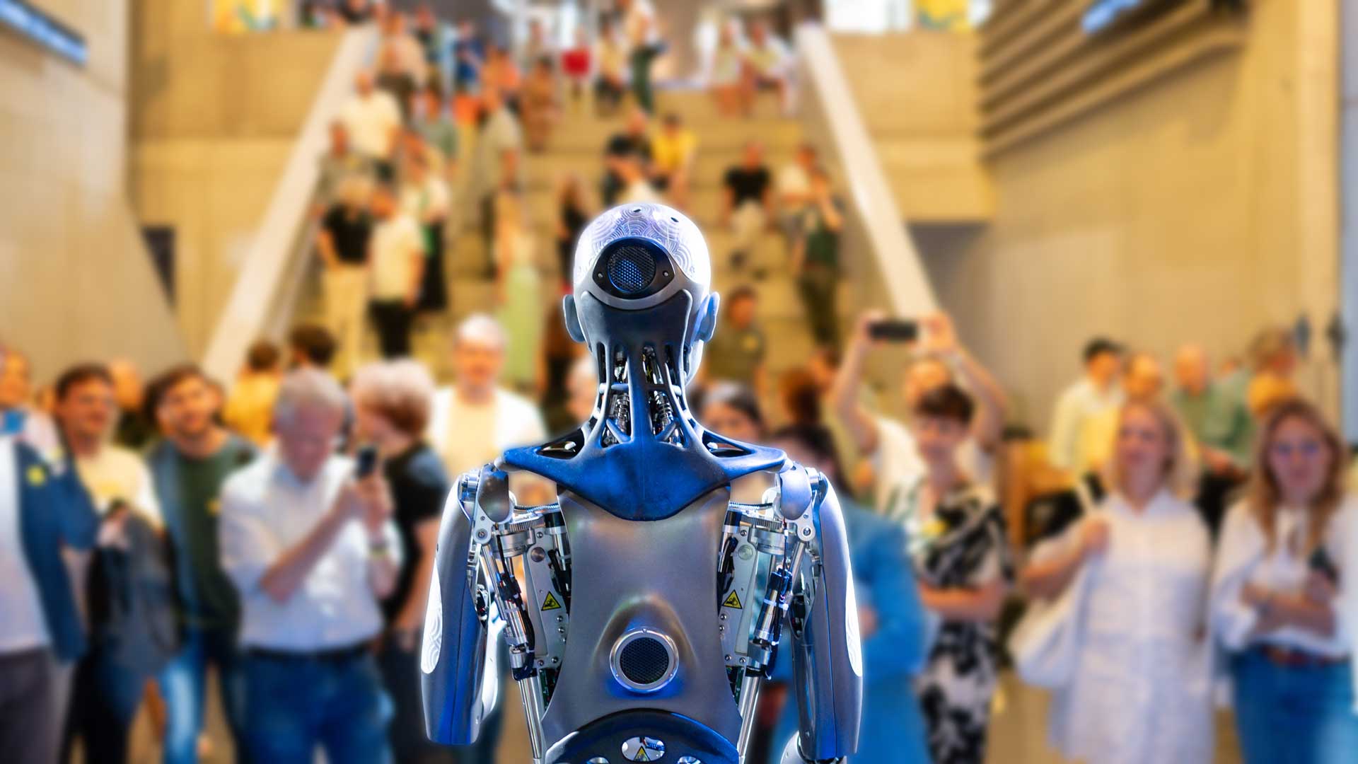 Humanoid robot "Ameca" with blue-silver casing in front of blurry audience